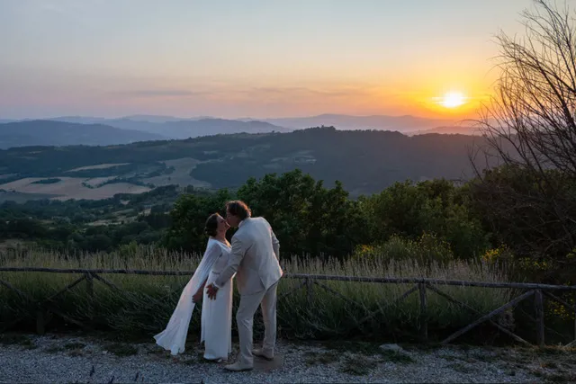 real-bride-review-daphne-de-laat-bruidshuis-diana – bruid Daphne de Laat en haar bruidegom kussen elkaar bij een adembenemend uitzicht over glooiende heuvels tijdens zonsondergang