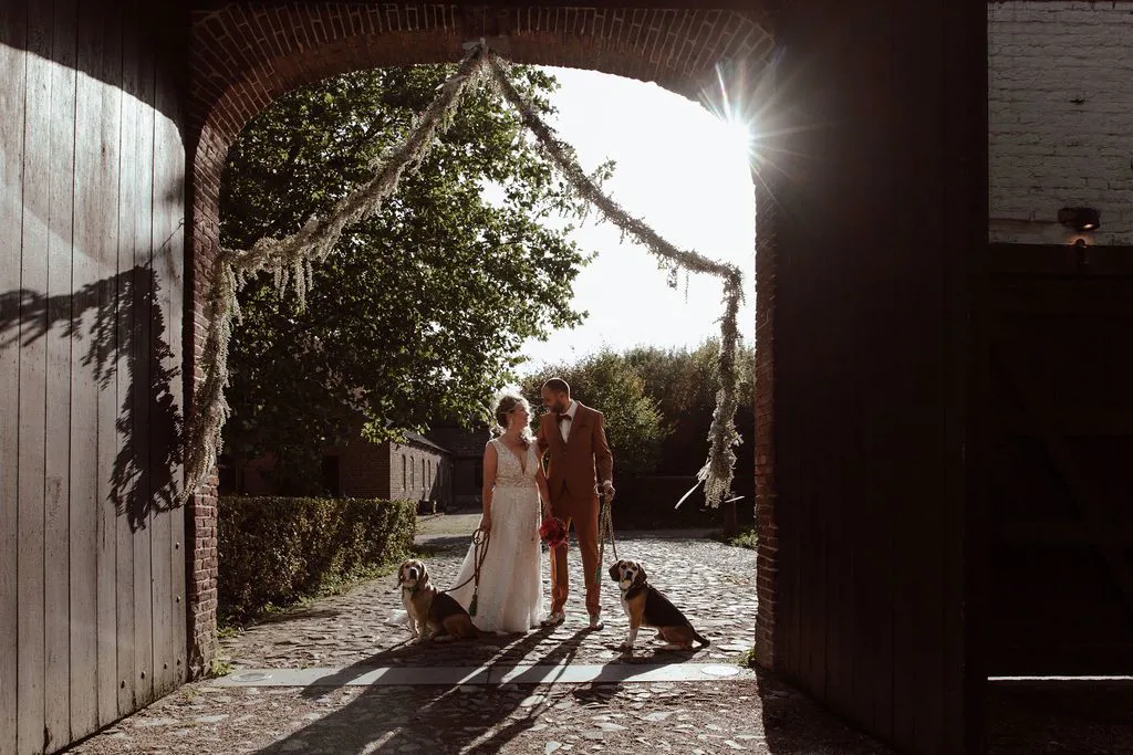 11.	Real bride Mandy Gout en Vincent wandelen samen met hun honden onder een feestelijk versierde poort. 
