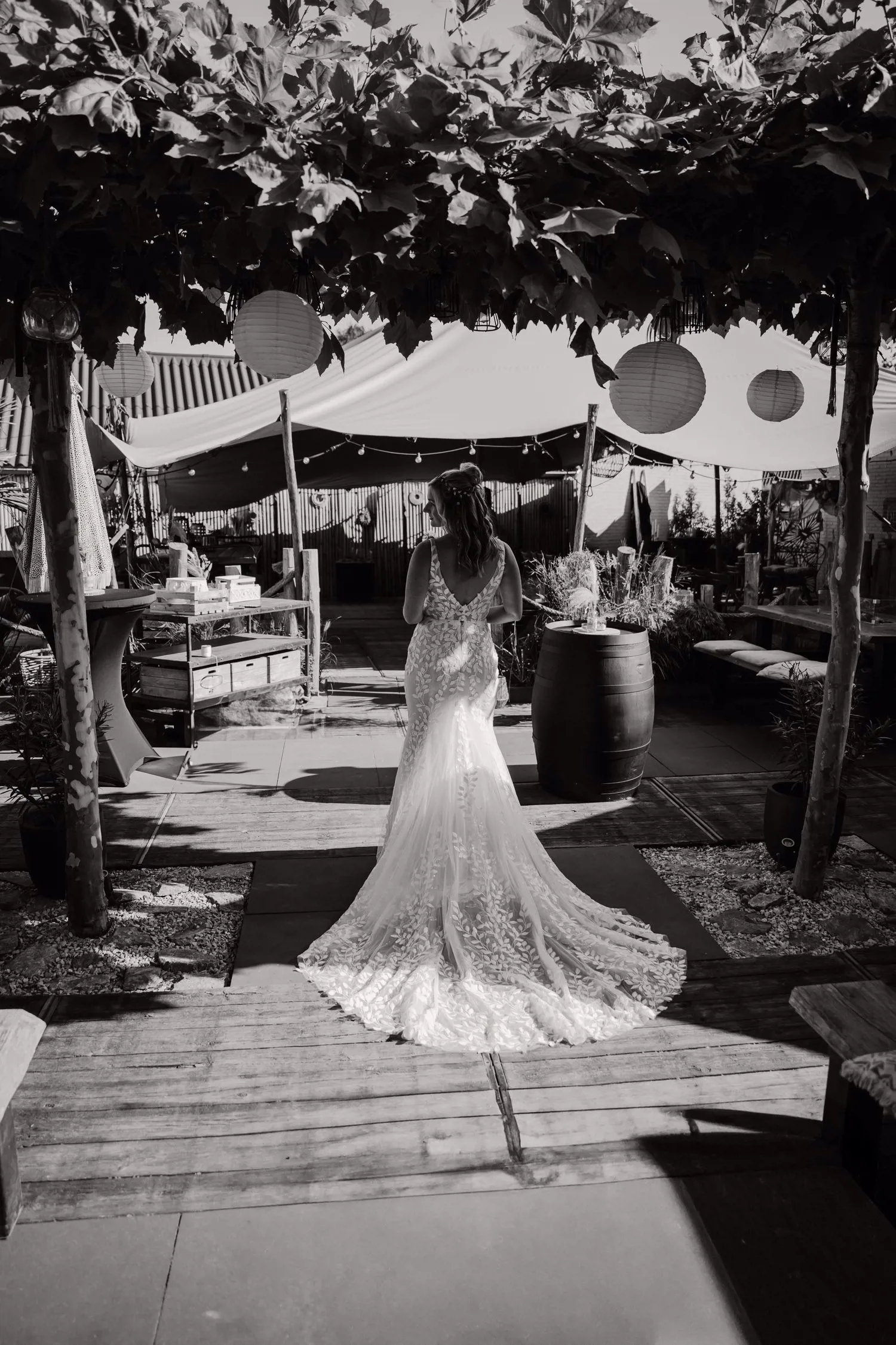 Real bride Lisa van Dooren loopt buiten onder een pergola, in een fit & flare jurk met kanten rug en sleep.