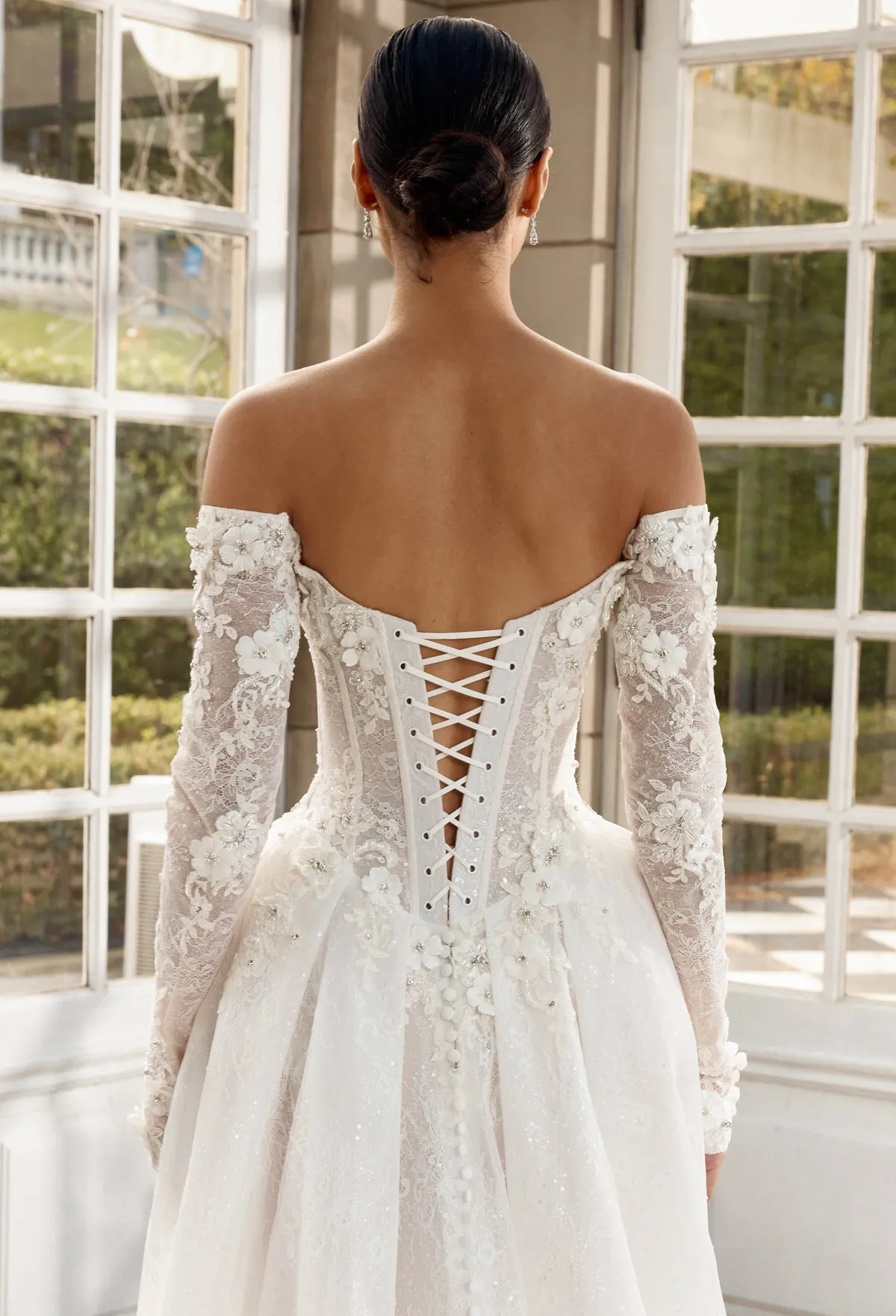 Off-shoulder trouwjurk Italia met 3D kant. Achteraanzicht met korset en lange mouwen van Jeune by Madi Lane.