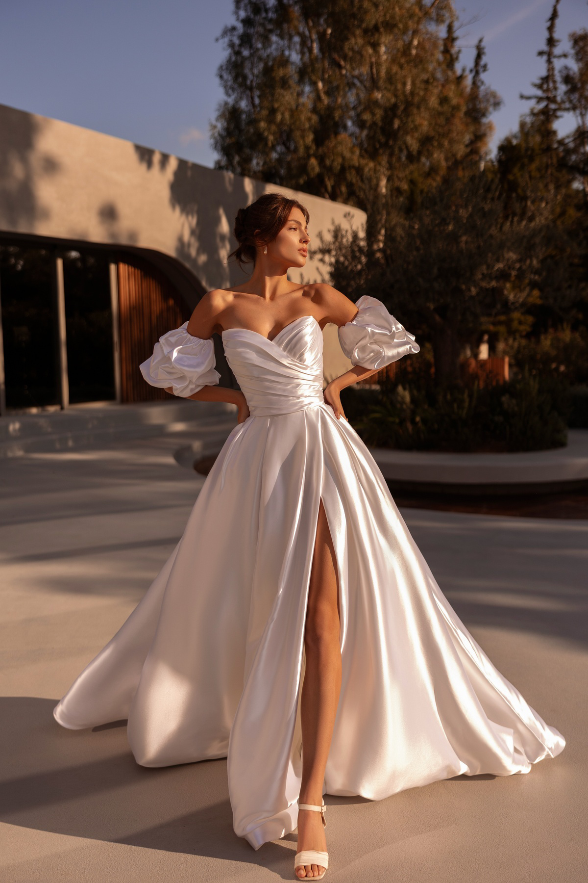 Off-shoulder A-lijn trouwjurk 1525 van Demetrios met split. Vooraanzicht van het satijnen gedrapeerde lijfje en pofmouwen.