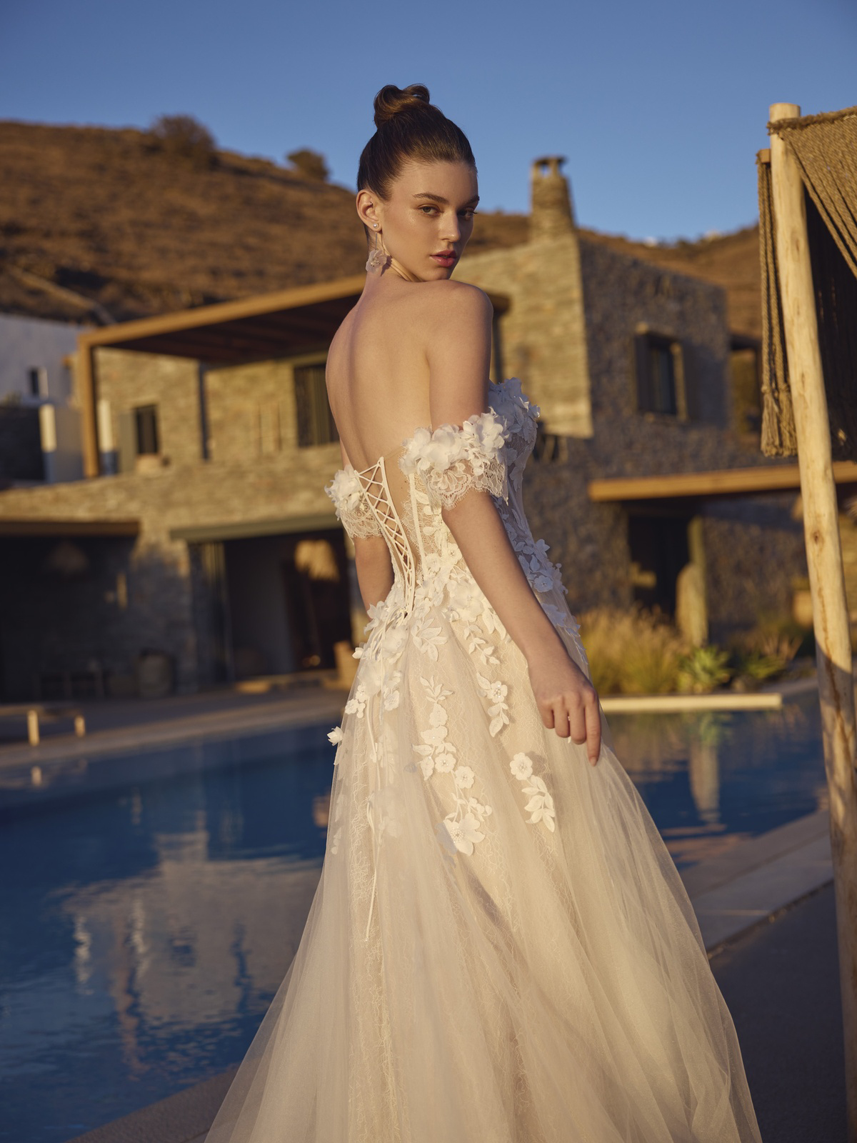 Off-shoulder trouwjurk Halia van Modeca met A-lijn. Achteraanzicht van de open rug met korsetsluiting en 3D bloemen.