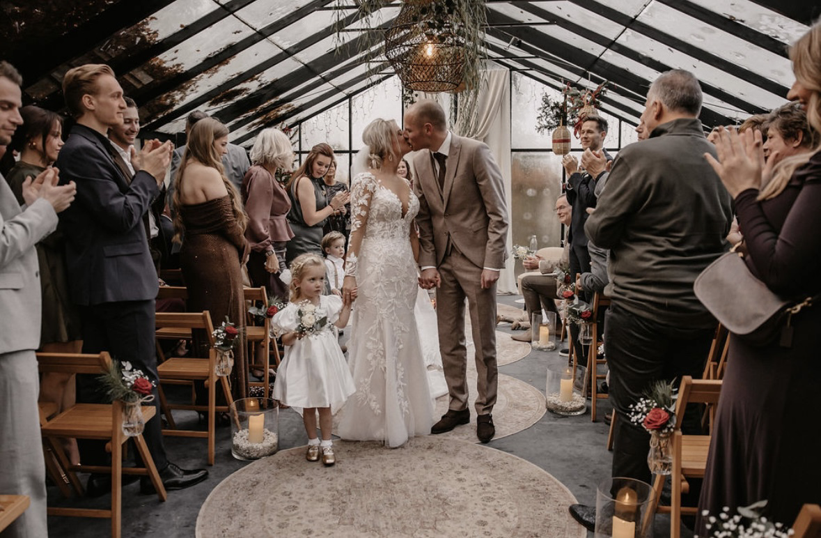 real-bride-review-celine-altena-eijsermans-bruidshuis-diana – bruid Celine Altena-Eijsermans en haar bruidegom lopen hand in hand door het gangpad terwijl gasten applaudisseren