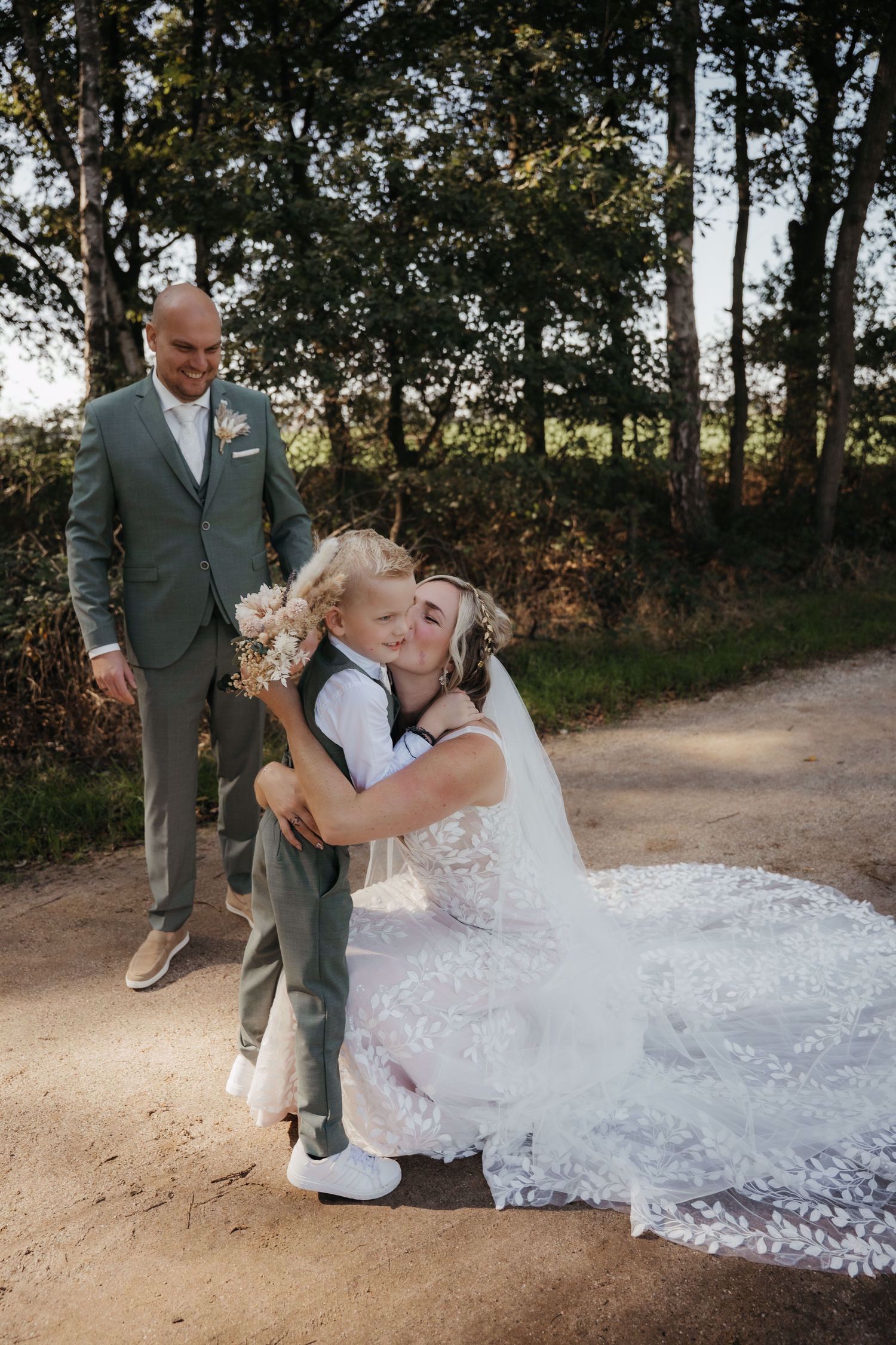 Real bride Lisa van Dooren knielt met haar kind, in een romantische fit & flare jurk met lange sluier.