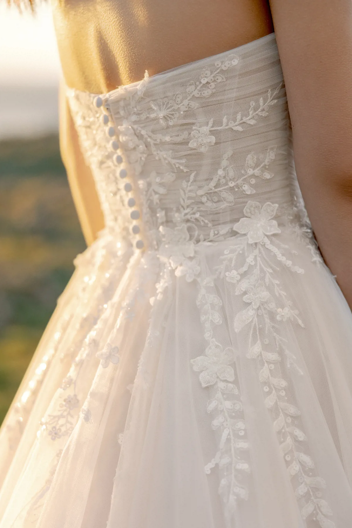Strapless trouwjurk 11424 Adore, close-up achteraanzicht. Detail van het lijfje met bloemenkant, glitter en knoopjes.