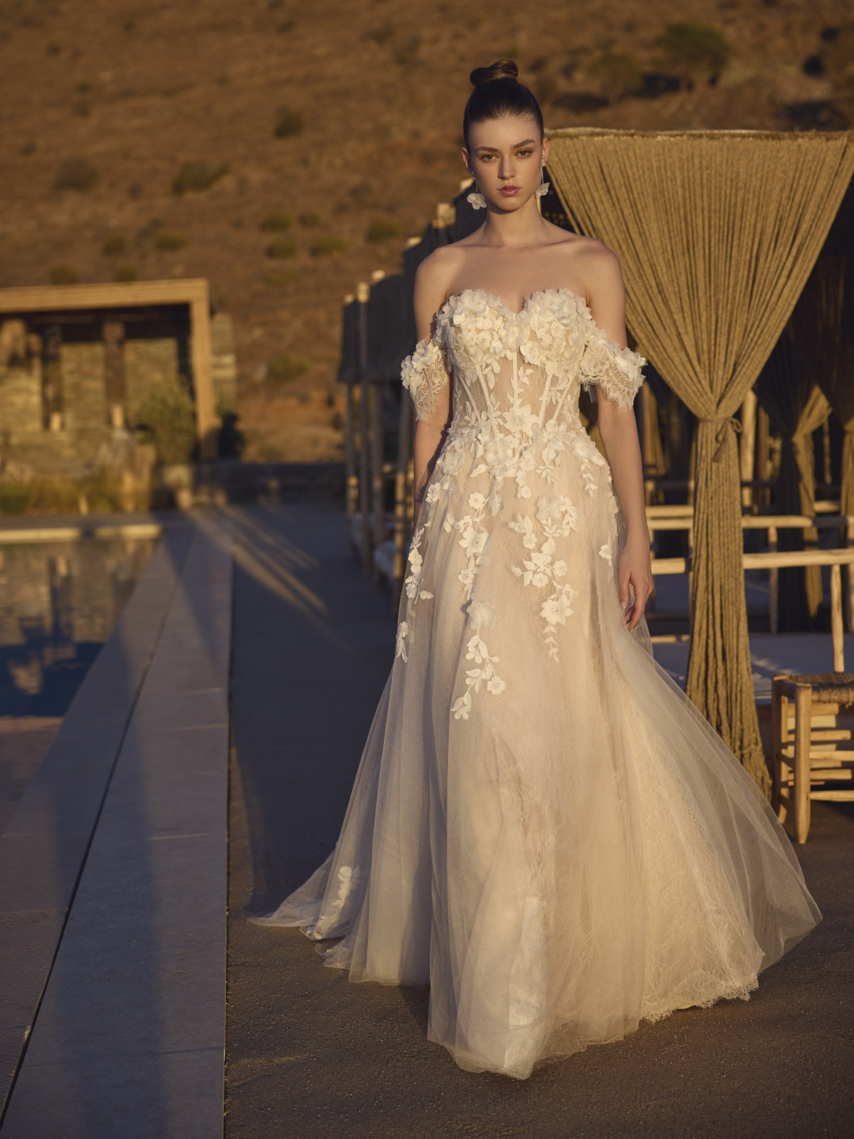 Off-shoulder trouwjurk Halia van Modeca met 3D kant en korsetlijfje in vooraanzicht. Romantische A-lijn bruidsjurk.