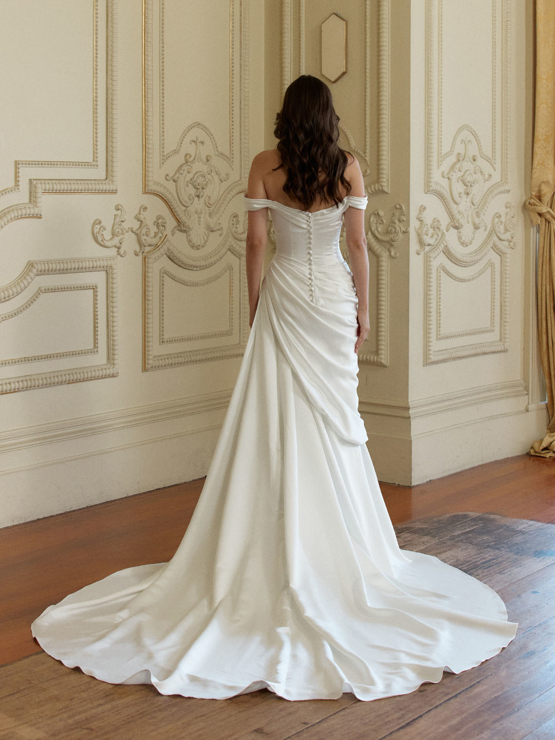 Off-shoulder trouwjurk Mora van Jeune by Madi Lane in satijn. Achteraanzicht met picpac knoopjes en gedrapeerde rok.