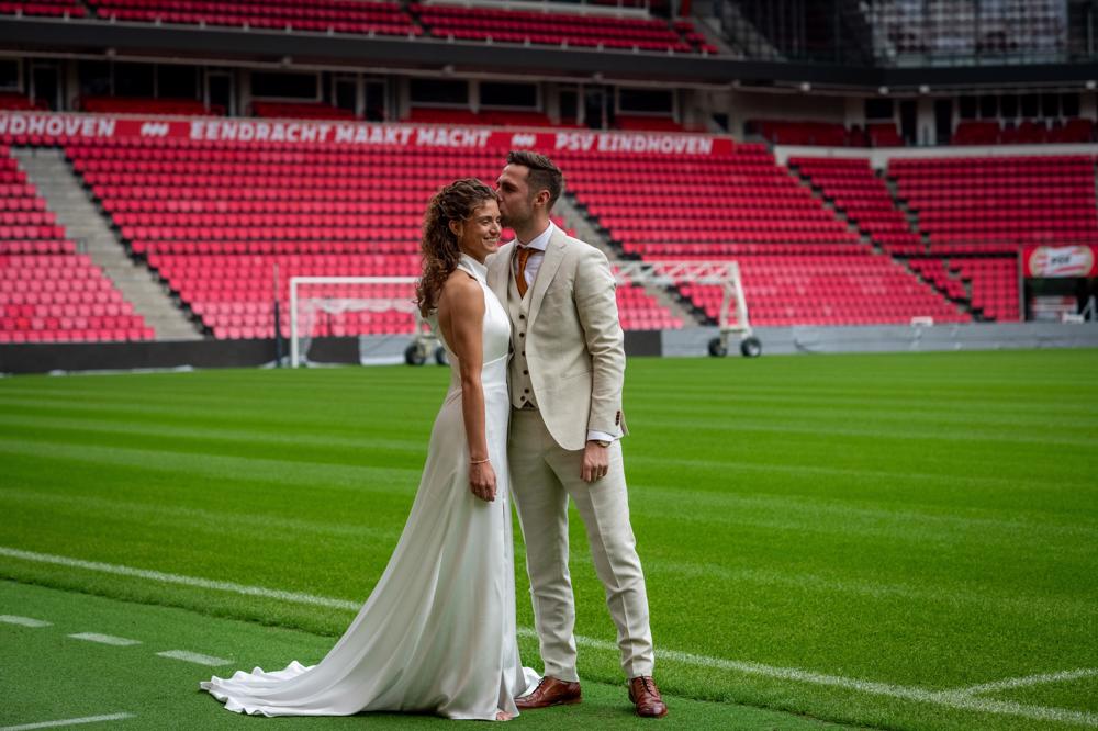 real bride robin verbeek in een elegante fit and flare trouwjurk samen met haar bruidegom op het veld van het psv stadion