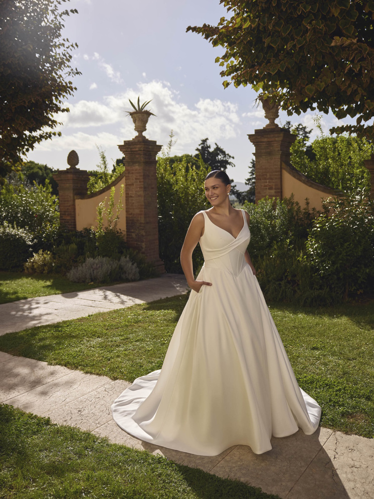 A-lijn trouwjurk Janneke van Modeca. Zijaanzicht van de satijnen jurk met gedrapeerd lijfje met baleinen en V-hals.