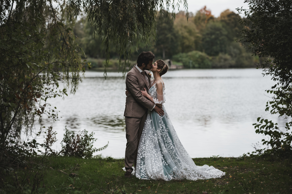 real bride Lauren van der Genugten in een unieke trouwjurk met verfijnde bladerenapplicaties, romantisch moment met haar bruidegom aan het water