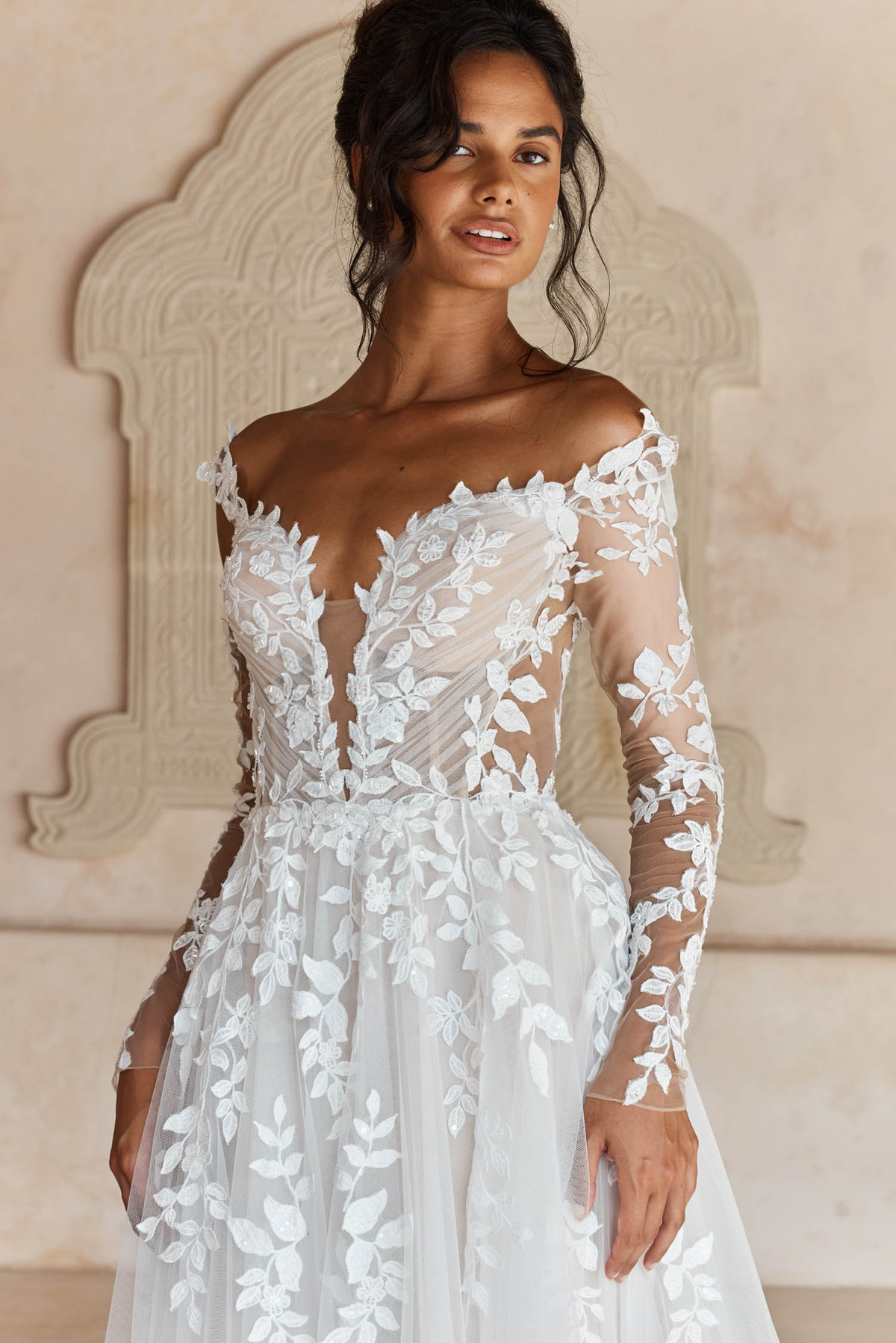 Off-shoulder trouwjurk Landon van Madi Lane met kanten lange mouwen en diepe V-hals, close-up van het lijfje.