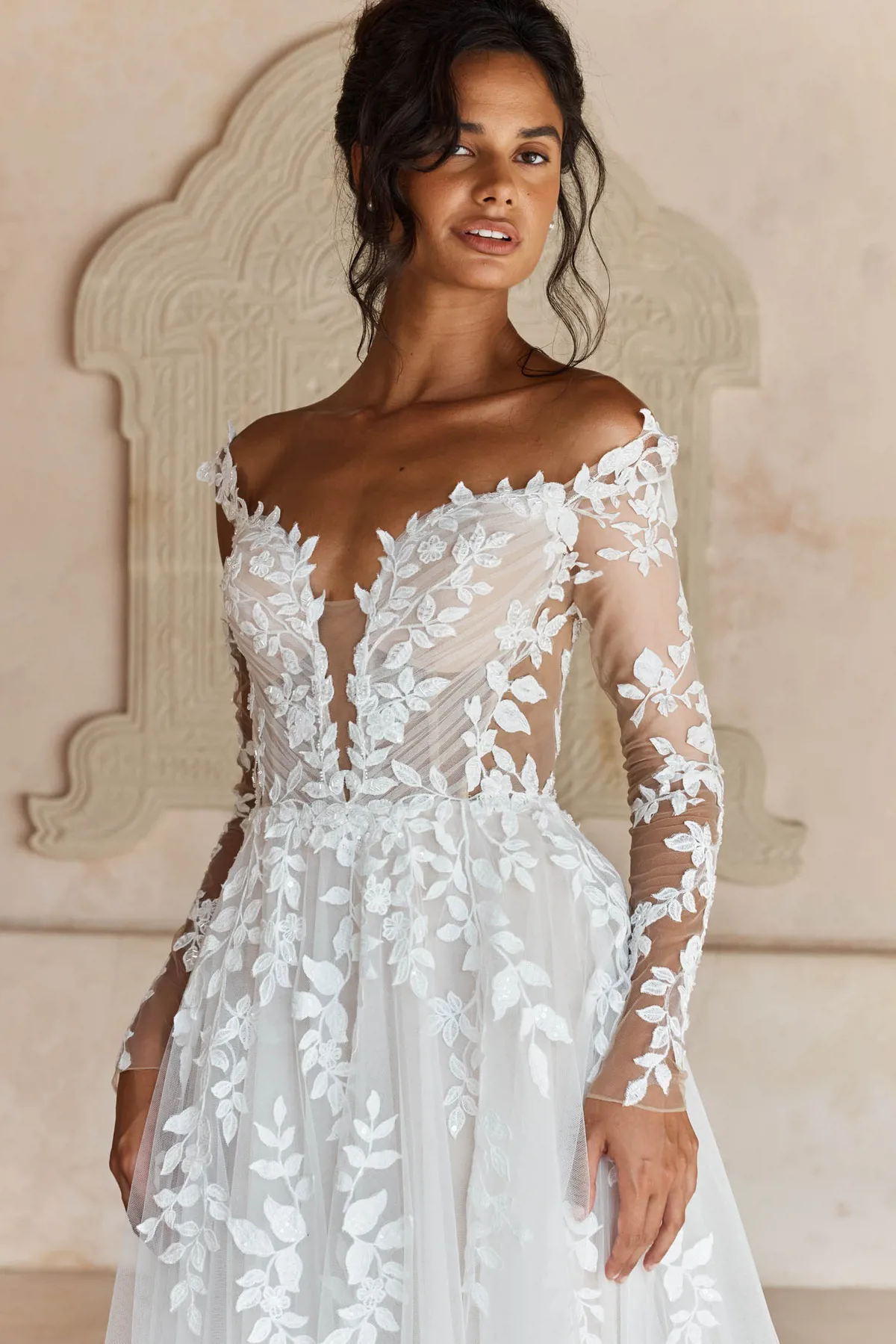 Off-shoulder trouwjurk Landon van Madi Lane met kanten lange mouwen en diepe V-hals, close-up van het lijfje.