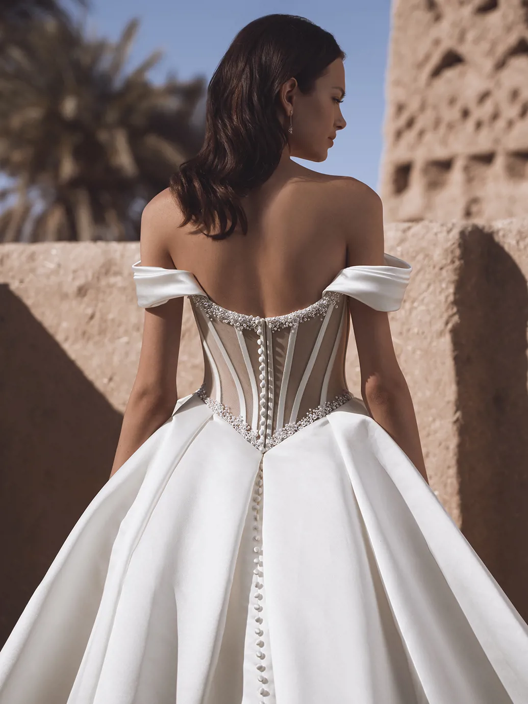 Off-shoulder trouwjurk Temina Blue by Enzoani, achteraanzicht met see-through korsetlijfje en wijde satijnen rok met parels.