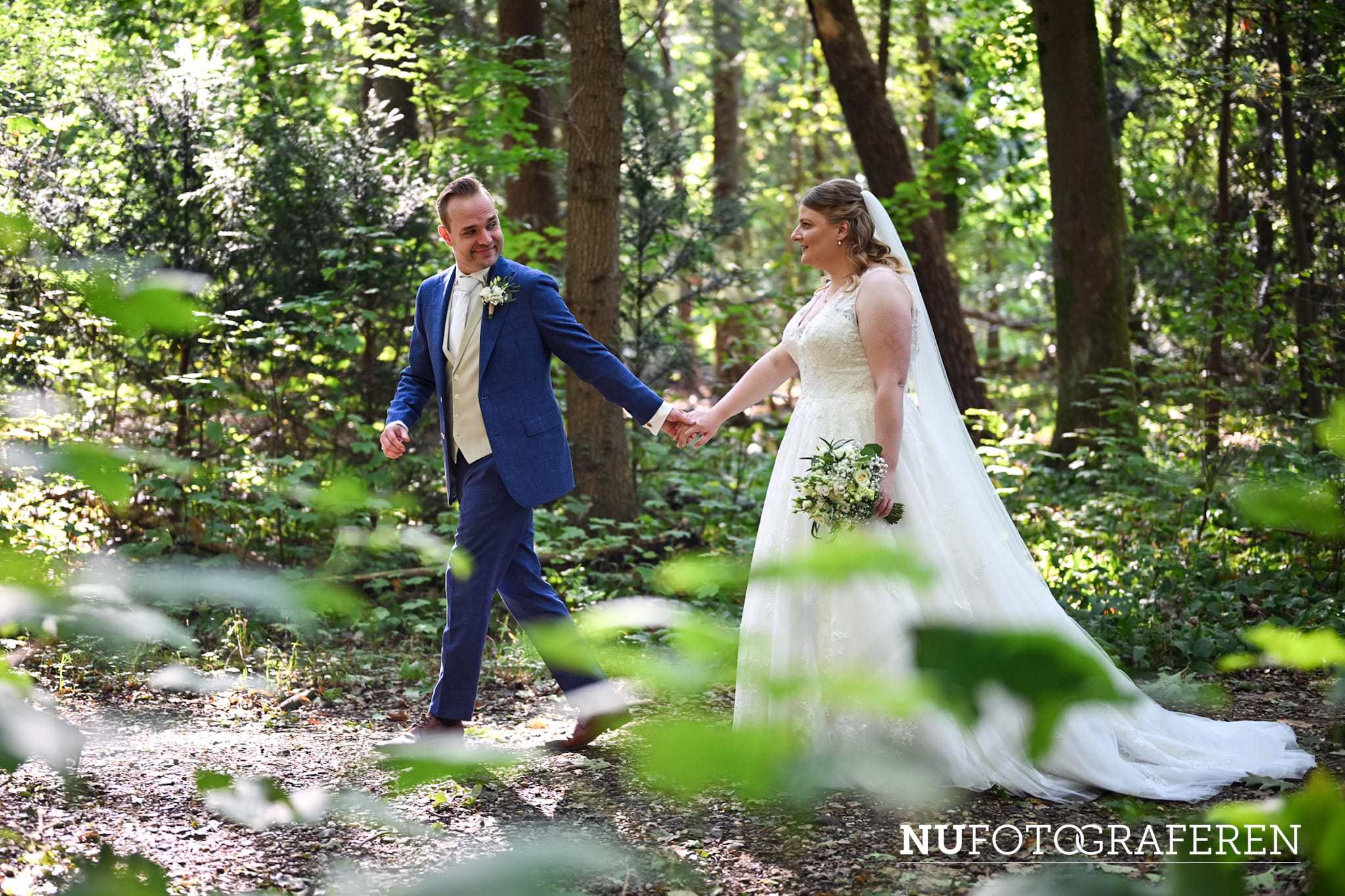 Bruid Stefanie Hegelsom wandelt hand in hand met haar bruidegom door het bos en draagt een romantische trouwjurk van Bruidshuis Diana.