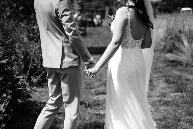 real bride rosanne – romantische A-lijn trouwjurk met kanten rugdetails en zachte tule rok – bruid en bruidegom lopen hand in hand door een zonnige, natuurlijke buitenlocatie (zwart-wit foto)