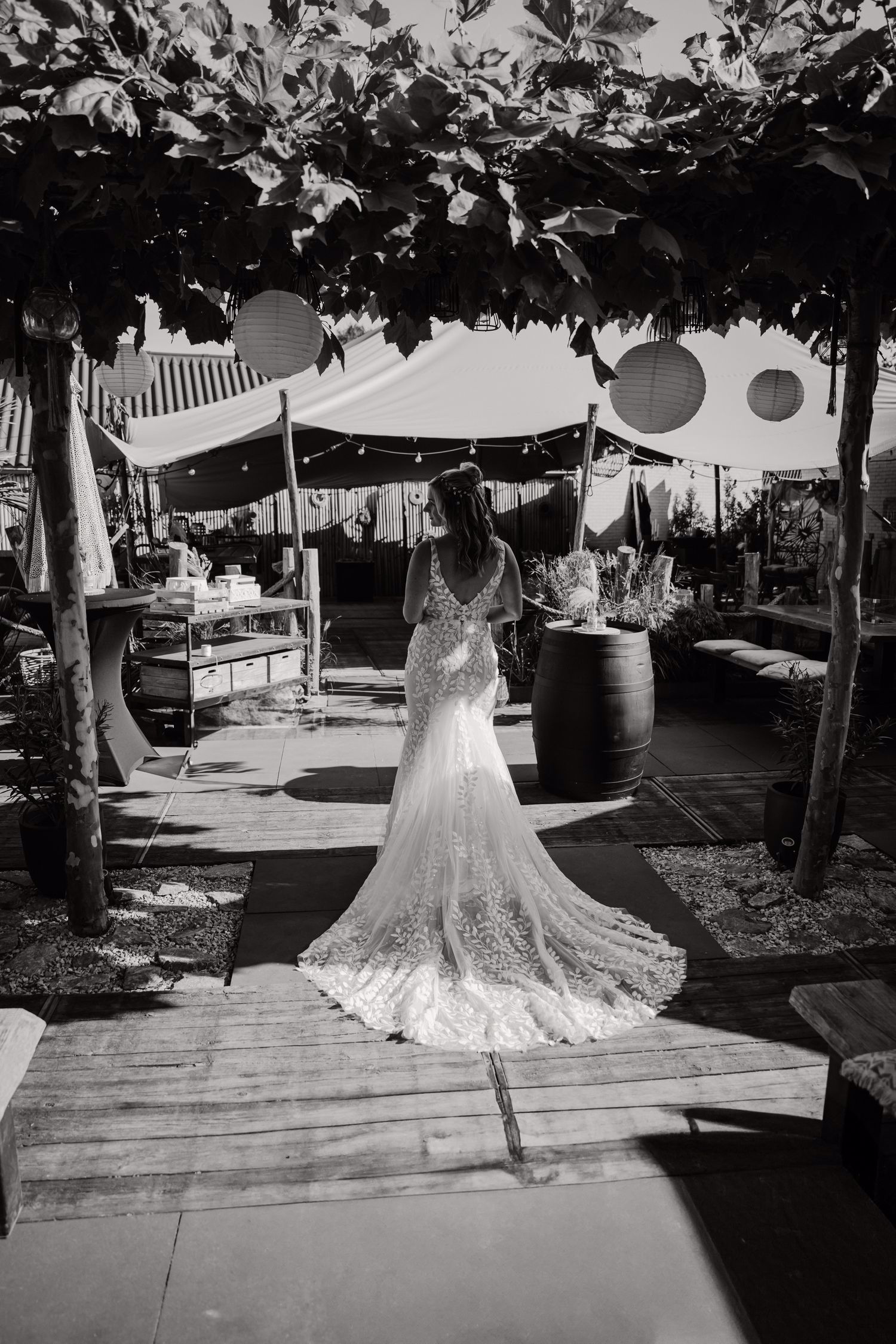 Real bride Lisa van Dooren loopt buiten onder een pergola, in een fit & flare jurk met kanten rug en sleep.
