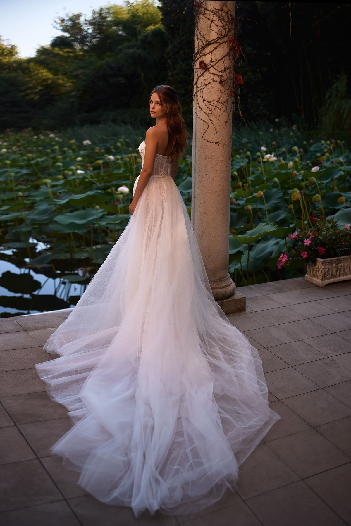 Romantische A-lijn trouwjurk Keenley van Milla Nova LR. Achteraanzicht met strapless korsetlijfje en lange tule sleep.