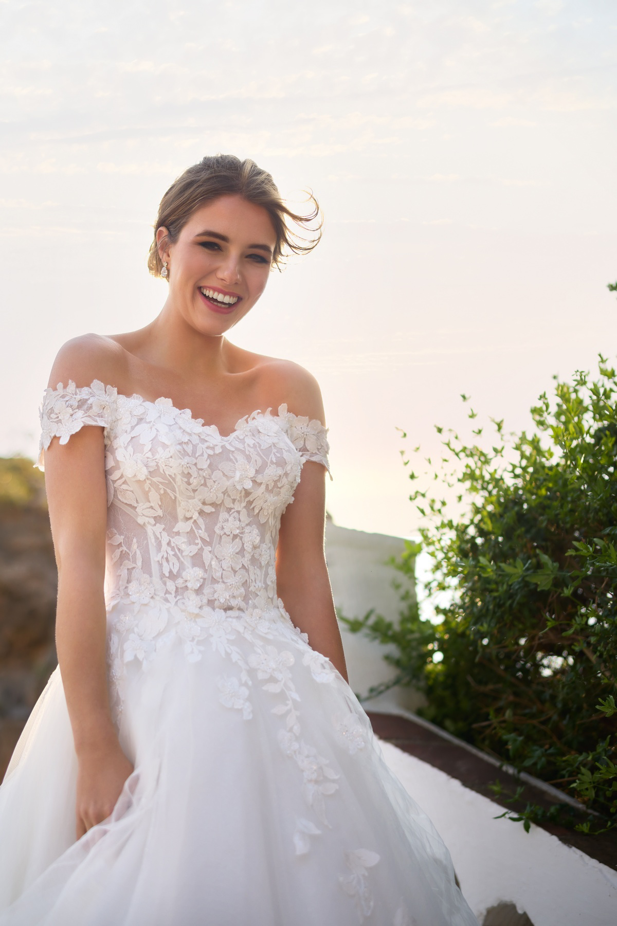 Off-shoulder trouwjurk 26206 van Tres chic met 3D kant en een see-through korsetlijfje. Close-up van lachende bruid.