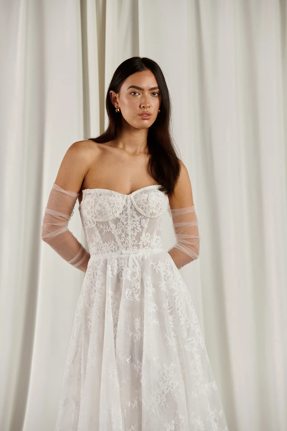 Kanten A-lijn trouwjurk 23203 van Cizzy Bridal. Vooraanzicht met strapless korsetlijfje en losse tule mouwen.