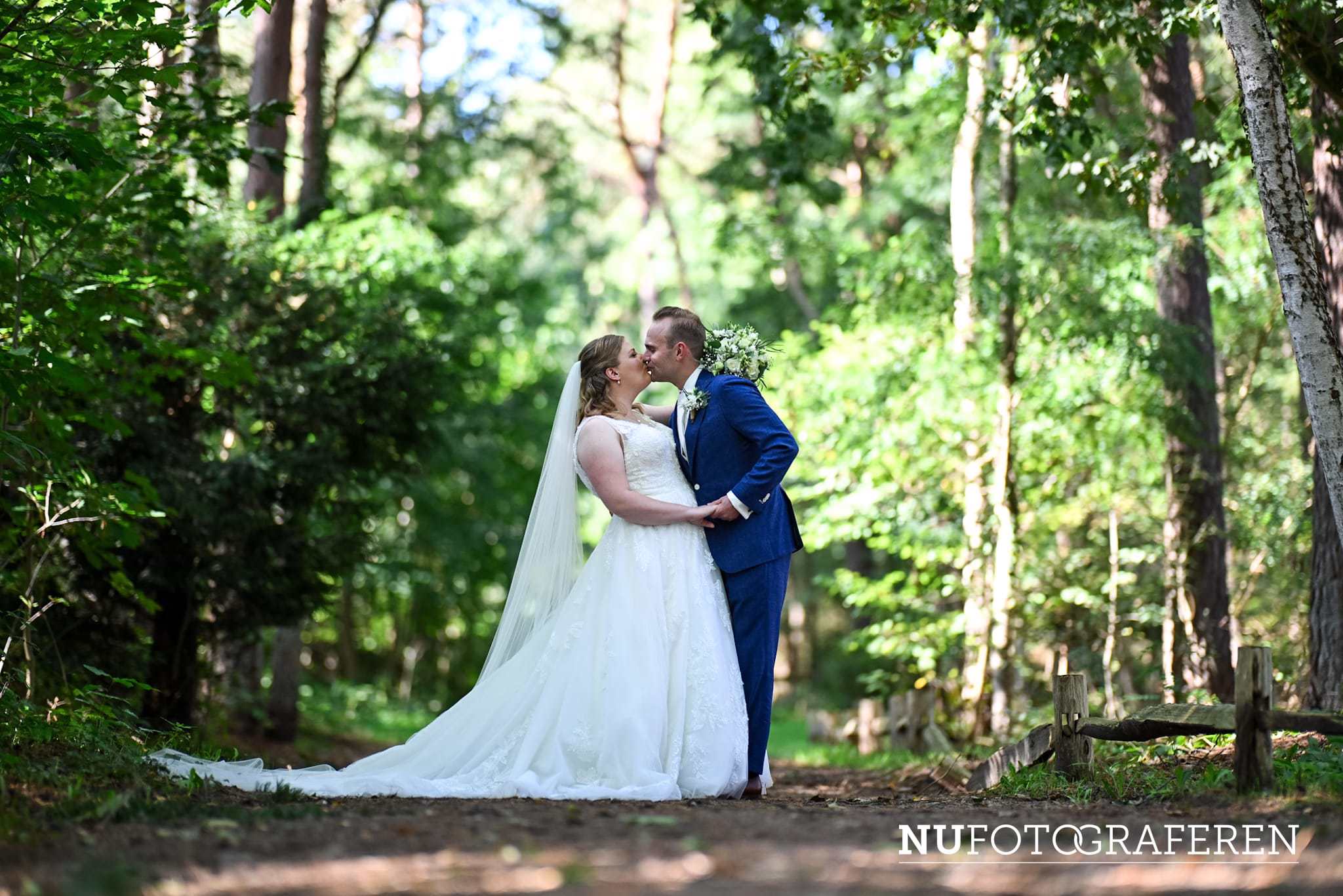 Bruid Stefanie Hegelsom deelt een kus met haar bruidegom in een groene bosrijke omgeving en draagt een elegante trouwjurk van Bruidshuis Diana