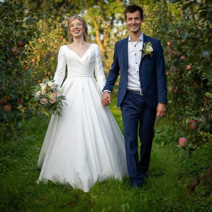real bride Jessica Blom Aperloo hand in hand met haar partner in een boomgaard, frisse en romantische setting