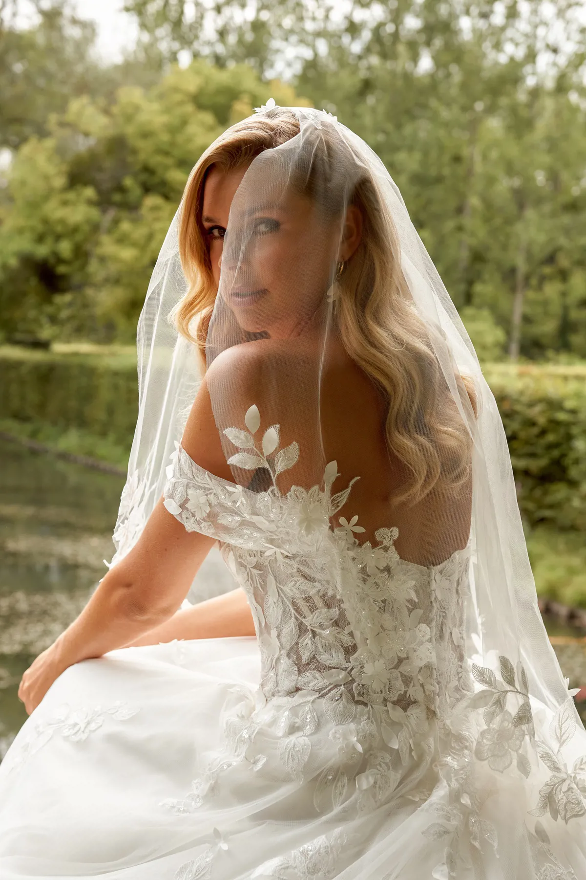 Off-shoulder trouwjurk 44520 van Sincerity Bridal, achteraanzicht met see-through lijfje en 3D kanten bloemen.