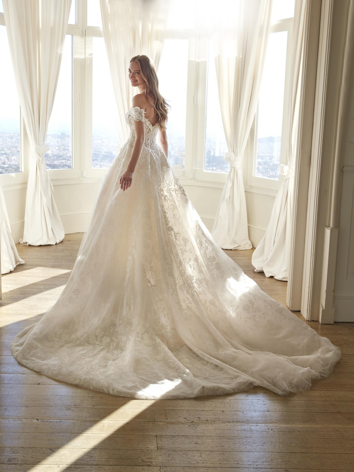 Off-shoulder trouwjurk Juddy van San Patrick met lange sleep. Achteraanzicht van de romantische prinsessenjurk met kant.