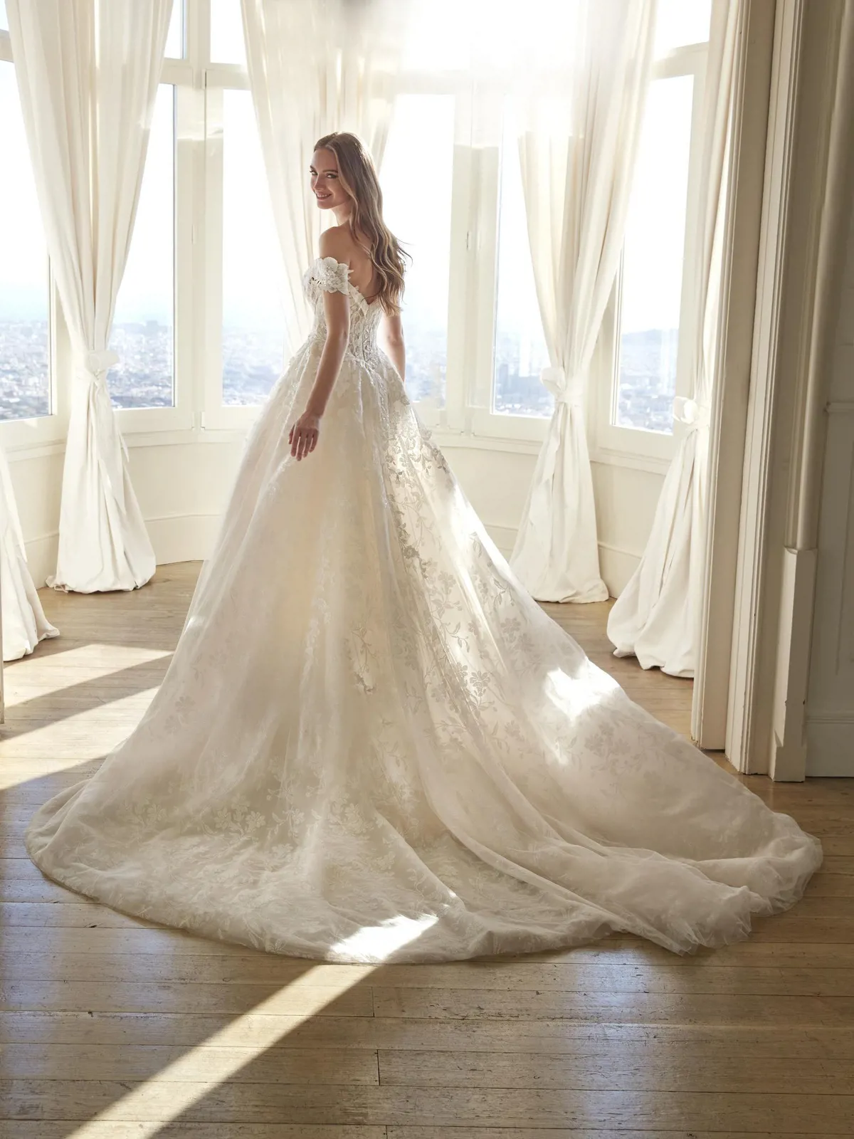 Off-shoulder trouwjurk Juddy van San Patrick met lange sleep. Achteraanzicht van de romantische prinsessenjurk met kant.