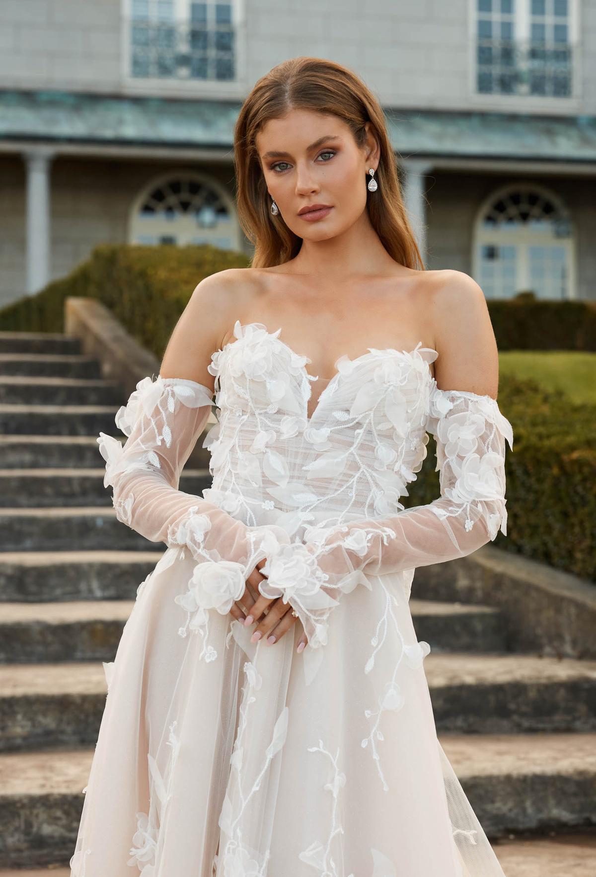 Off-shoulder trouwjurk Juno van Jeune by Madi Lane met 3D bloemen op een romantisch korsetlijfje. Vooraanzicht.