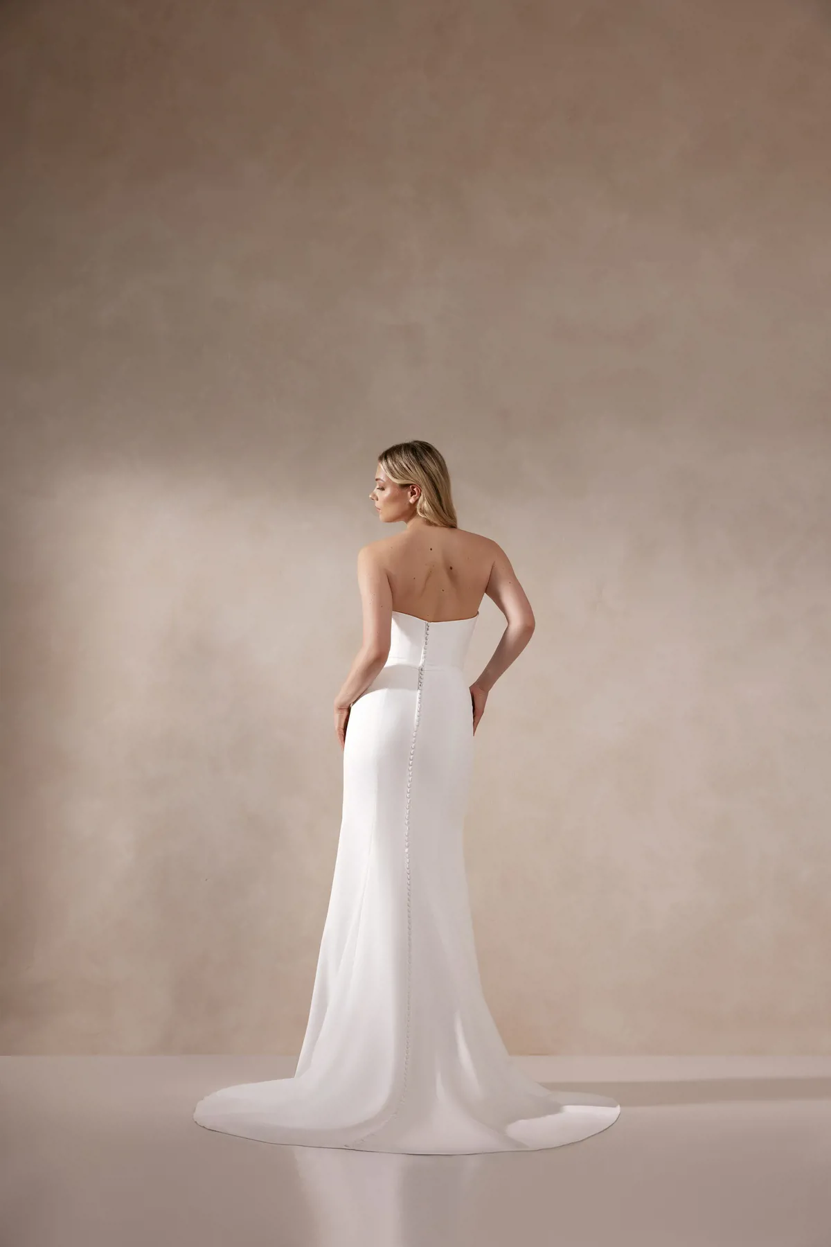 Aangesloten bruidsjurk Adore Deva. Achteraanzicht van de strapless trouwjurk met een lage rug en picpac knoopjes.