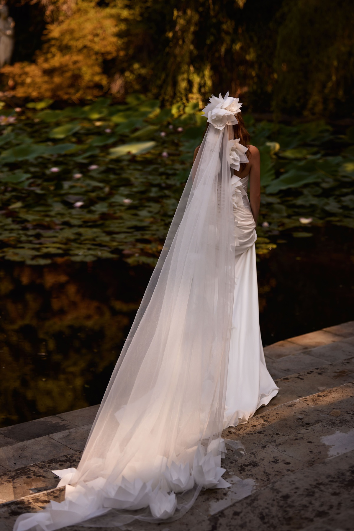 Trouwjurk met lage rug Amika van Milla Nova LR. Achteraanzicht van de aangesloten jurk met gedrapeerd satijn en 3D bloemen.