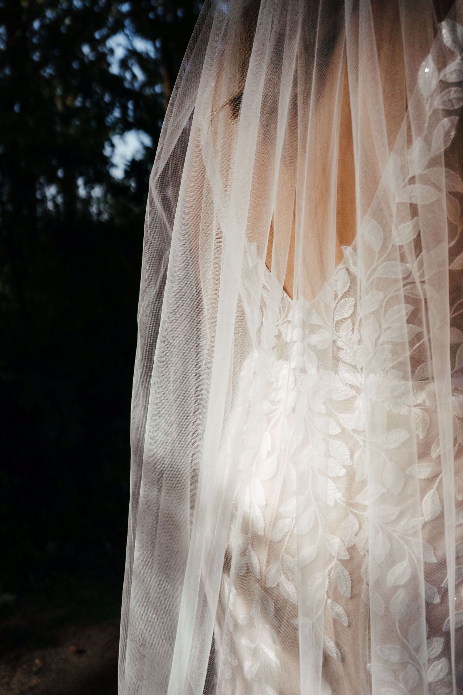 Real bride Lisa van Dooren close-up van de rug, in een romantische fit & flare jurk met bladkant en sluier.