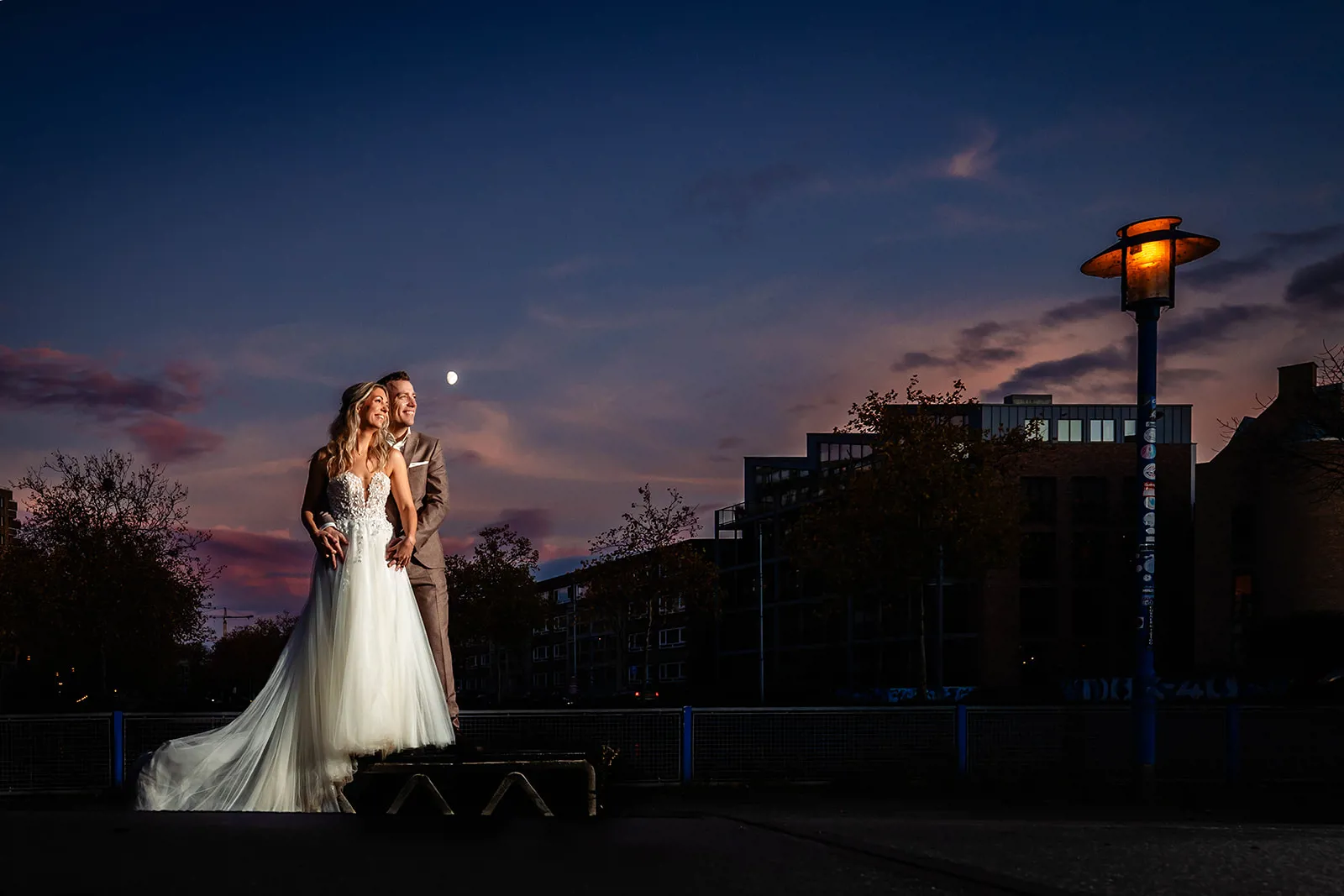Bruid Candy Mulder staat samen met haar bruidegom tijdens een romantische avondshoot bij zonsondergang, zij draagt een elegante trouwjurk van Bruidshuis Diana.