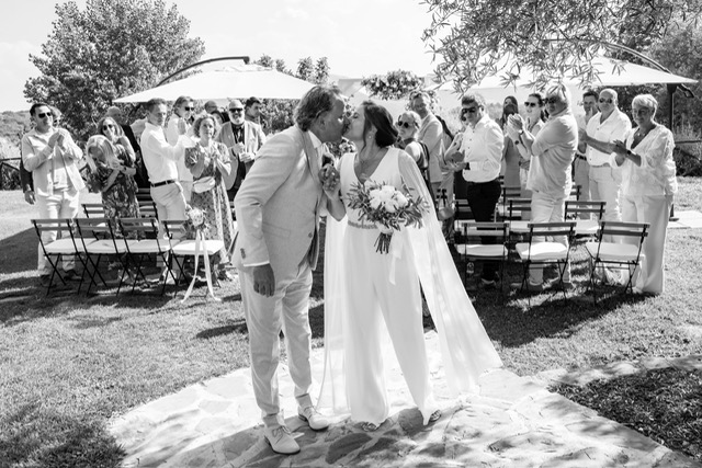 real-bride-review-daphne-de-laat-bruidshuis-diana – bruid Daphne de Laat in een elegante ivoorkleurige jumpsuit met cape mouwen loopt hand in hand met haar bruidegom een stenen trap af tijdens hun bruiloft