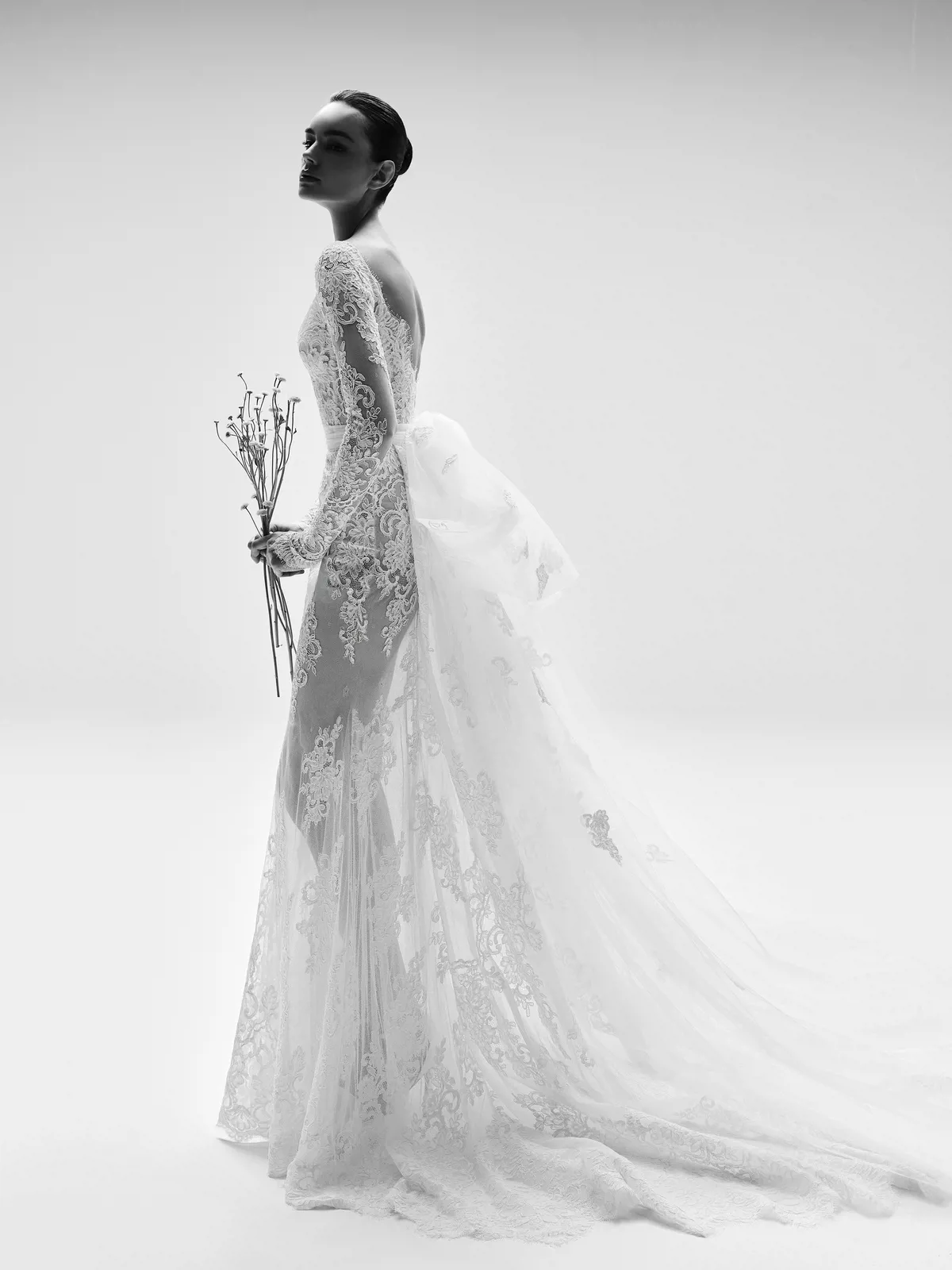 Kanten see-through trouwjurk Yvanna van Zuhair Murad. Zijaanzicht van de bruidsjurk met lange mouwen en een open rug.