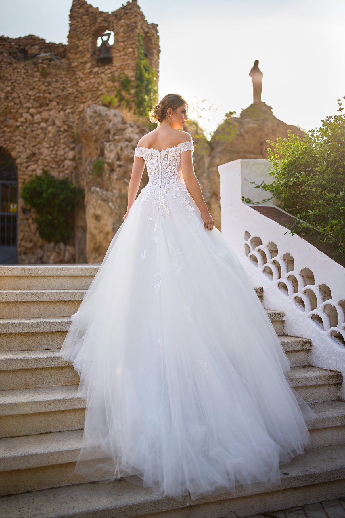 Prinsessen trouwjurk 26206 van Tres chic met off-shoulder top. Achteraanzicht van het kanten lijfje en de wijde tule rok.