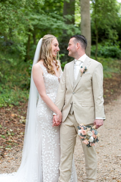 Real Bride Savannah – bruid en bruidegom tegenover elkaar bij historische locatie; bruid in aangesloten kanten trouwjurk met elegante sleep.