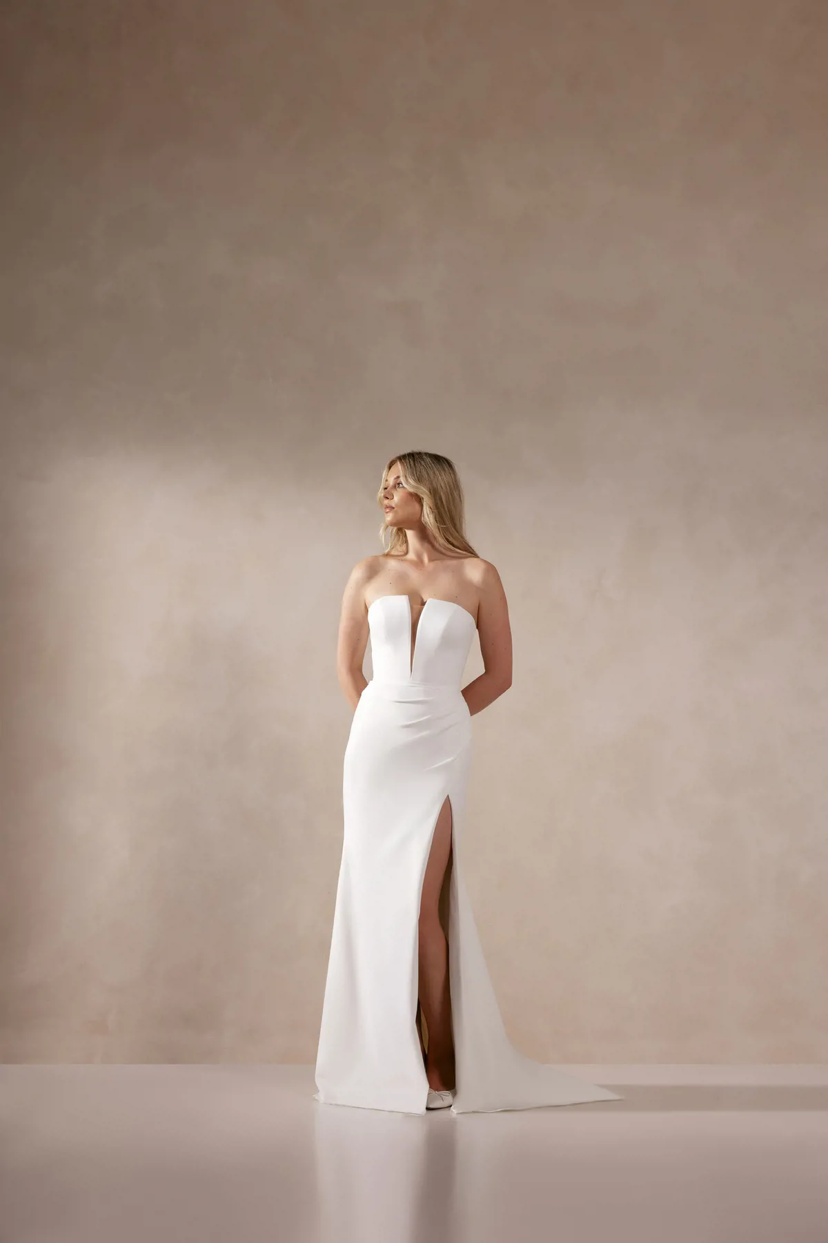 Trouwjurk met split Deva van Adore. Vooraanzicht van de strapless, minimalistische bruidsjurk met diepe V-hals.