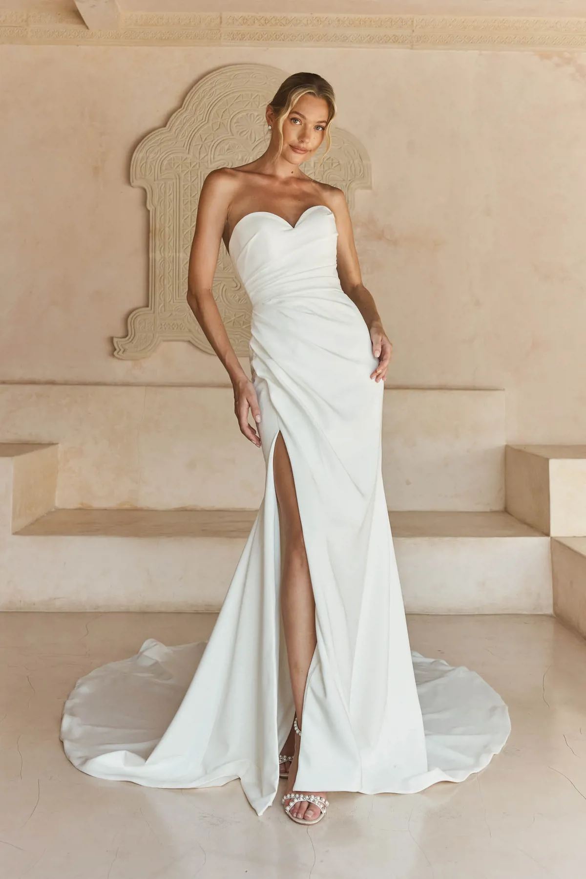 Strapless trouwjurk Libbi van Madi Lane met hoge split en gedrapeerd lijfje. Vooraanzicht van de minimalistische bruidsjurk.