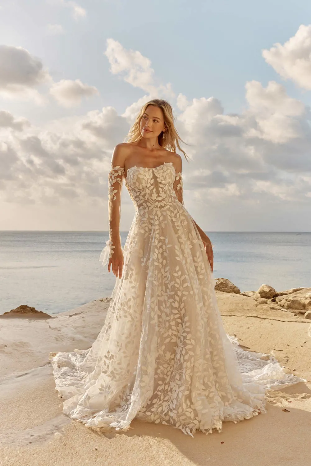Off-shoulder bruidsjurk Laiya van Madi Lane. Vooraanzicht A-lijn met korsetlijfje, bladkant en lange see-through mouwen.